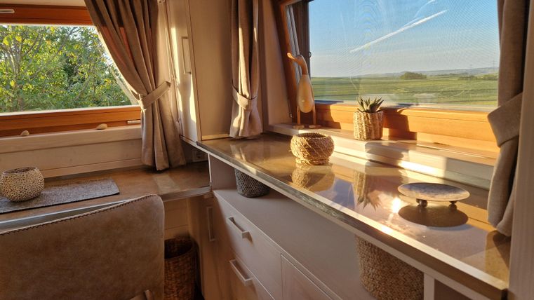 Ein heller, einladender Wohnraum mit großen Fenstern und gemütlicher Einrichtung. Auf der Fensterbank stehen Pflanzen und dekorative Gegenstände.