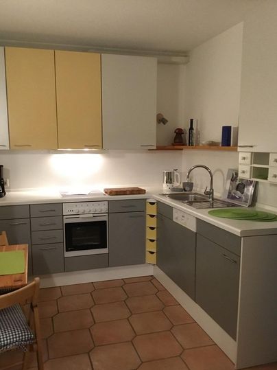 Eine moderne Küche mit grauen und gelben Schränken. Sie ist gut ausgestattet mit einem Herd, einem Waschbecken und einer gemütlichen Sitzecke.