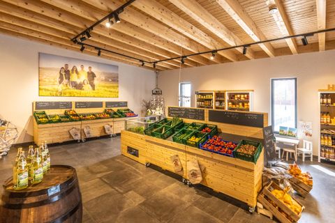 Ein gemütlicher Verkaufsraum mit Holzregalen und frischem Obst und Gemüse. Im Hintergrund befindet sich ein großes Wandbild mit einer ländlichen Szene.