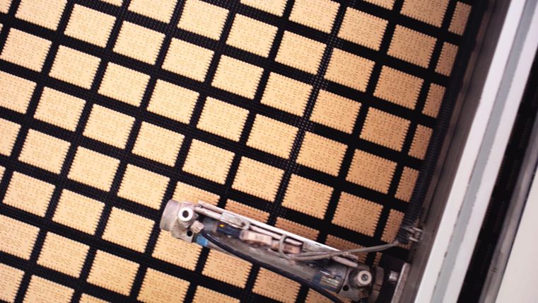 Ein quadratischer Bodenbelag mit einem schwarz-beigen Muster ist zu sehen. Am Rand befindet sich eine Reinigungsmaschine.