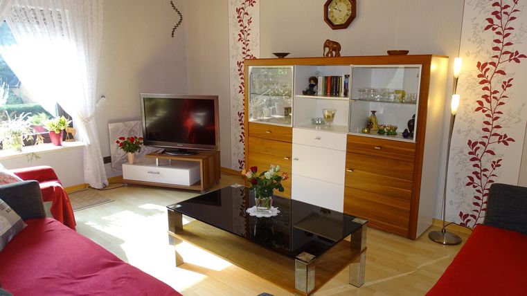 Een gezellige woonkamer met rode en grijze banken. De glazen salontafel staat voor een tv-kast en een paar decoratieve planten.