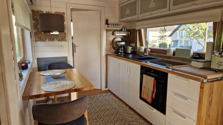 Eine moderne Küche mit hellen Holzmöbeln und einer großen Fensterfront. Am Tisch stehen zwei Stühle und es gibt verschiedene Küchengeräte.