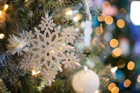 Eine schöne silberne Schneeflockenornament hängt an einem Weihnachtsbaum. Der Hintergrund ist mit bunten Lichtern geschmückt.