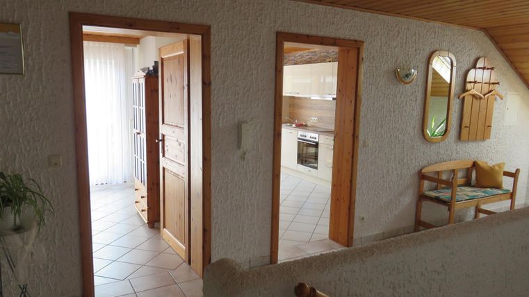 Ein heller Flur mit offenen Türen zu anderen Räumen. Rechts steht eine kleine Sitzgelegenheit und ein Spiegel an der Wand.