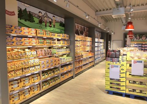 Ein gut sortierter Lebensmittelladen mit Regalen voller Verpackungen. Die Wände sind hell und modern gestaltet, mit bunten Produkten in unterschiedlichen Kategorien.