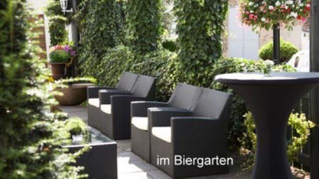 Eine gemütliche Biergarten-Ecke mit schwarzen Rattanmöbeln und grünen Pflanzen. Ein eleganter Stehtisch ergänzt die entspannte Atmosphäre.
