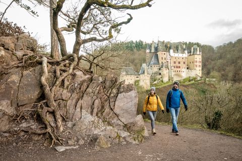 Zwei Wanderer auf einem Pfad mit Burg Eltz im Hintergrund.