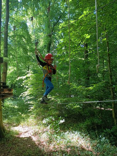 Ein Kind, das an einer Seilrutsche im Wald schwingt. Der Bereich ist grün und voller Bäume.