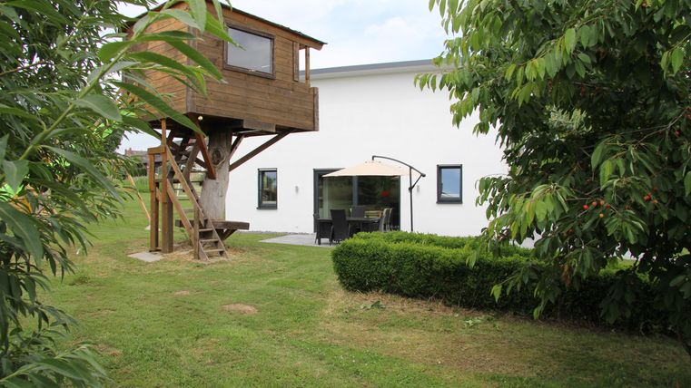 Une maison moderne avec une maison de jeu dans le jardin. L'extérieur est verdoyant et accueillant, avec une terrasse et des meubles.