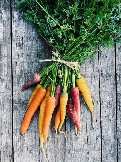 Ein Bund bunter Karotten liegt auf einem Holztablett. Die Karotten haben verschiedene Farben und sind frisch mit grünem Laub verbunden.