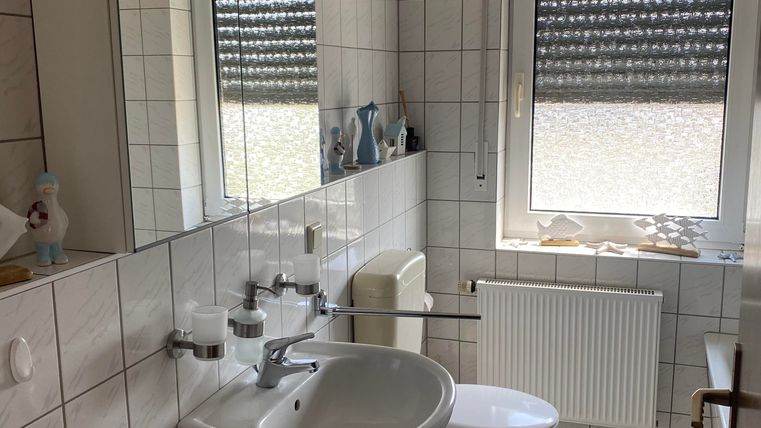 Ein modernes Badezimmer mit weißen Fliesen und einem großen Spiegel. Es verfügt über ein Waschbecken, eine Toilette und ein Fenster mit Sicht nach außen.