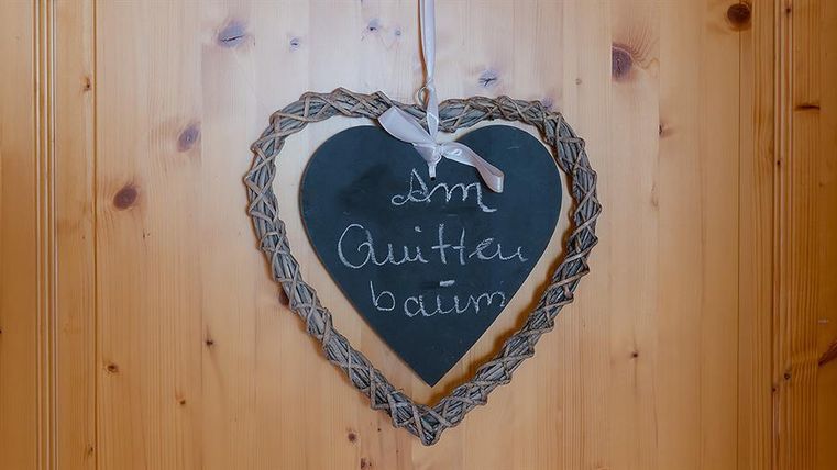 Ein herzförmiges Schild aus Holz mit der Aufschrift „Am Gütlauer Baum“. Das Schild ist an einer Holzwand befestigt.