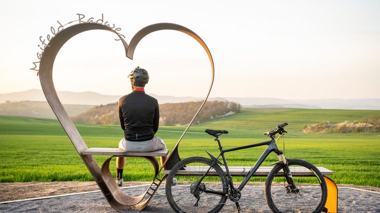 Ein Radfahrer blickt in die Ferne, er sitzt auf der Schatzbank am Maifeld-Radweg