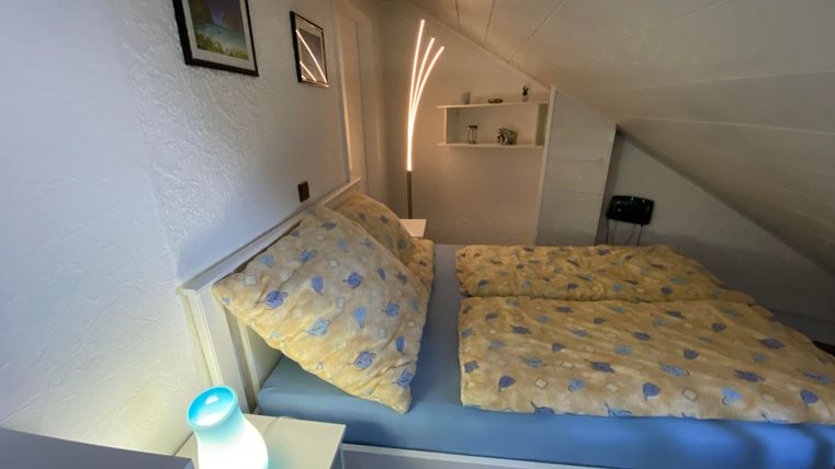 Ein gemütliches Schlafzimmer mit einem Doppelbett und bunten Bettdecken. Es gibt eine moderne Lampe und einige Bilder an der Wand.