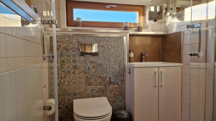 Ein modernes Badezimmer mit einer Dusche und einer Toilette. Die Wände sind teilweise gefliest und es gibt viel natürliches Licht durch das Fenster.