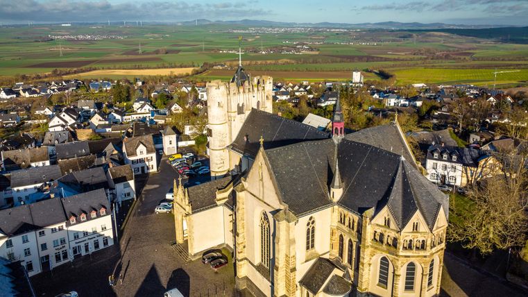 Une église historique entourée de vieux bâtiments et d'un paysage pittoresque. À l'arrière-plan, on peut voir des collines douces et un ciel clair.
