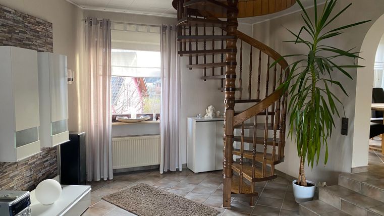 Ein heller Eingangsbereich mit einer Holzspiralte Treppe. Die Wände sind in sanften Farben gehalten und es steht eine große Pflanze in der Ecke.