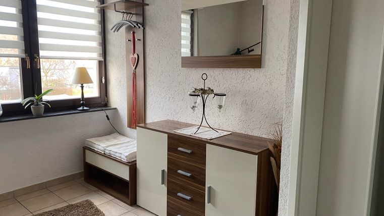 Ein moderner Flur mit einem Schuhschrank und einem großen Spiegel. Helle Wände und Fenster sorgen für viel Tageslicht.