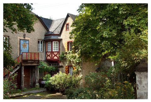 Ein charmantes Haus mit einer bunten Fassade und einem Balkon. Der Garten ist üppig und von Bäumen umgeben.