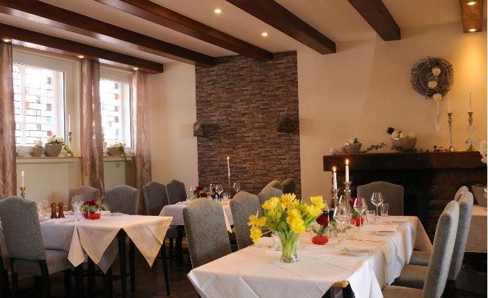 Ein elegantes Restaurant mit gedeckten Tischen und einem gemütlichen Ambiente. Die Wände sind mit Stein und Holzakzenten gestaltet, und Kerzen sorgen für eine angenehme Stimmung.