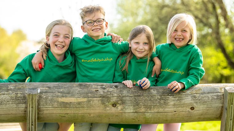 Vier Kinder lachen in die Kamera, sie tragen Hoodies mit dem Aufdruck #maifeldschätzje