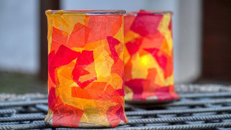 Zwei leuchtende Laternen mit buntem Papier in Rot- und Orangetönen. Sie stehen auf einem Gitterrost und strahlen warmes Licht aus.
