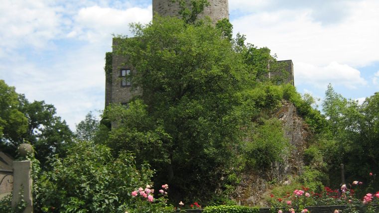 Ein alter Turm umgeben von lebhaften Pflanzen und Blumen. Der Himmel ist bewölkt und verleiht der Szenerie eine ruhige Atmosphäre.