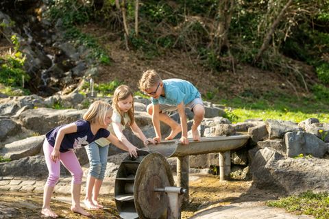 Kinder spielen an einem Wasserrad auf dem Wasserspielplatz am Maifeld-Radweg