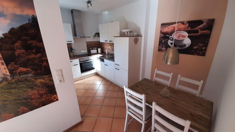 Une cuisine moderne avec une table à manger en bois et des chaises blanches. Sur le mur, il y a des images attrayantes et les meubles sont conçus de manière claire et accueillante.