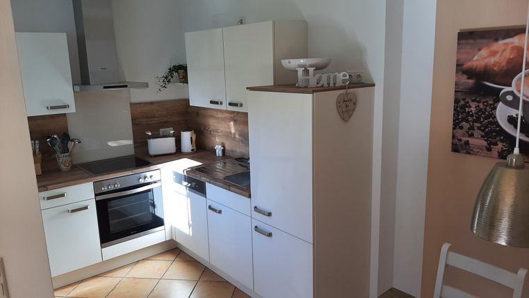 Une cuisine moderne avec des armoires blanches et des détails en bois. Sur le plan de travail se trouvent une cuisinière et un évier.