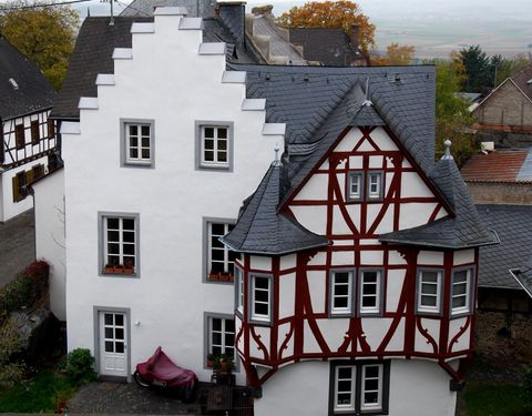 Ein traditionelles Fachwerkhaus mit weißen Wänden und einem roten Rahmengerüst. Das Dach ist dunkelgrau und die Fenster sind in einem klaren Design gehalten.