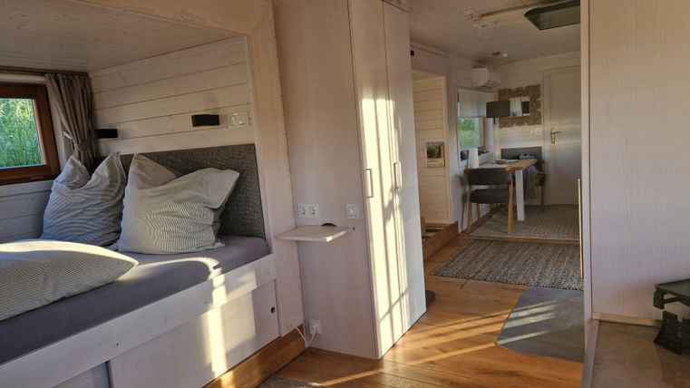 Ein heller und gemütlicher Innenraum mit einem Wohnbereich, der einen Schlafplatz und einen Tisch umfasst. Die Wände sind in sanften Farben gehalten und Holzfußböden verleihen ein warmes Ambiente.