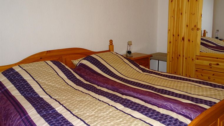 Ein gemütliches Schlafzimmer mit einem Holzbett und einem gestreiften Bettbezug. Im Hintergrund ist ein Spiegel und ein Bild an der Wand zu sehen.