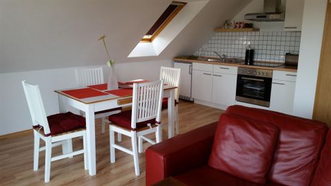 Une cuisine-salon confortable avec une table et des chaises blanches. La cuisine est moderne et bien équipée.