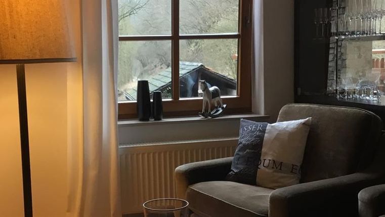 Ein gemütlicher Wohnbereich mit einem bequemen Sessel und einer Stehlampe. Durch das Fenster ist eine idyllische Landschaft sichtbar.