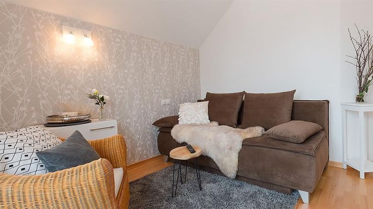 Ein gemütliches Wohnzimmer mit einer hellen, modernen Einrichtung. Der Raum enthält ein Sofa, einen kleinen Tisch und einen bequemen Stuhl.