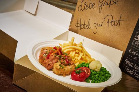 Ein leckeres Essen in einer Takeaway-Verpackung. Es enthält Fleisch, Pommes frites, Erbsen und Gemüse.