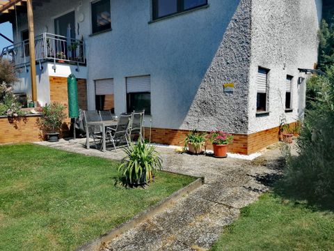 Ein Haus mit einem schönen Garten und einer Terrasse. Es gibt Gartenmöbel und einige Pflanzen.