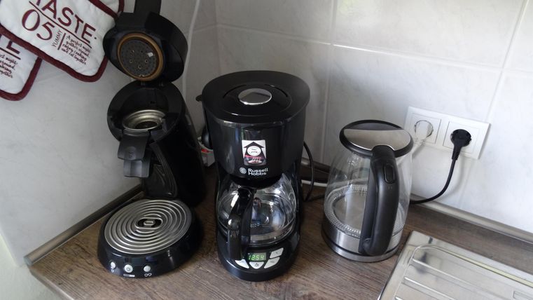 Eine moderne Kaffeemaschine steht auf einer Küchentheke. Neben ihr sind eine Wasserkocher und ein weiteres Küchengerät zu sehen.