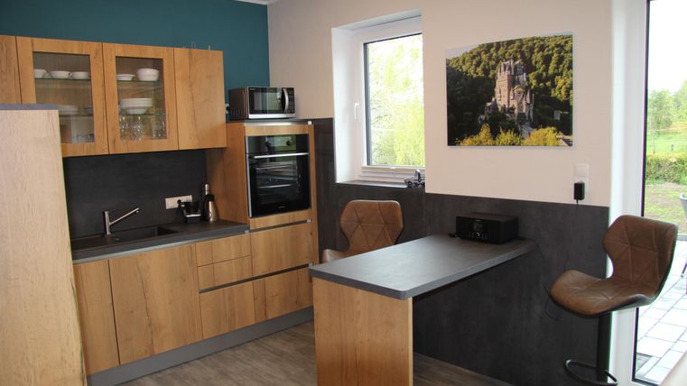 Une cuisine moderne avec des accents en bois et gris. Il y a un petit bar à manger et une fenêtre donnant sur la nature.