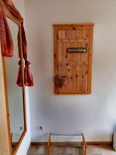 Ein einladender Eingangsbereich mit einem Holzschild, das "Herzlich Willkommen" sagt. Links befindet sich ein Spiegel und ein Holzregal.