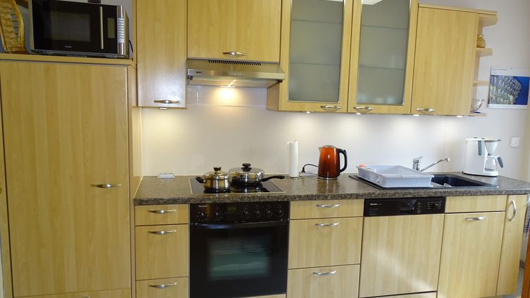 Een moderne keuken met houten meubels en witte muren. Er zijn apparaten zoals een fornuis, een magnetron en een gootsteen.