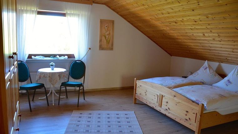 Ein gemütliches Zimmer mit Holzvertäfelung und zwei Einzelbetten. Es gibt einen kleinen Tisch mit Stühlen und viel Tageslicht durch das Fenster.