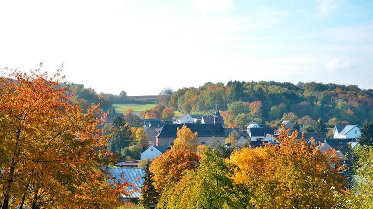 Ein malerisches Dorf im Herbst mit bunten Laubbäumen. Der Himmel ist klar und die Landschaft ist friedlich.