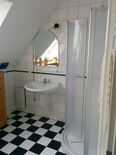 Ein modernes Badezimmer mit einer Dusche und einem Waschbecken. Der Boden ist im schwarz-weißen Schachmuster gestaltet.