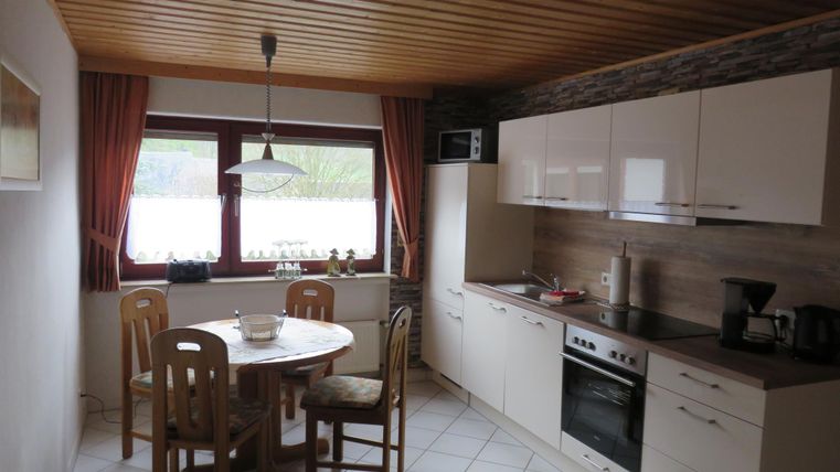 Eine helle Küche mit einem runden Tisch und vier Stühlen. Die Wände sind in einer neutralen Farbe gehalten, und die Fenster bieten einen Blick nach draußen.