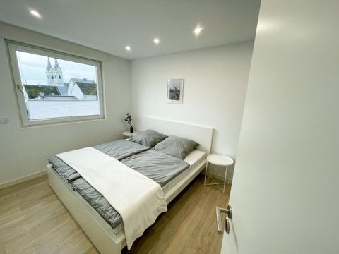 Ein modernes Schlafzimmer mit einem großen Doppelbett und neutralen Farben. Durch das Fenster ist ein Blick auf die Stadt zu sehen.