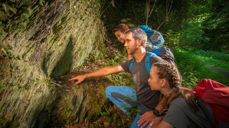 Drei Personen betrachten eine Felswand im Wald.