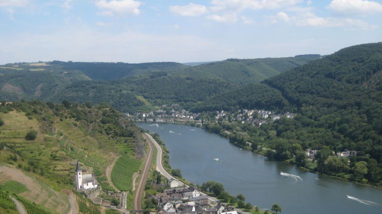 Eine malerische Flusslandschaft mit hügeligen Weinbergen und kleinen Dörfern. Der Himmel ist blau mit einigen Wolken.