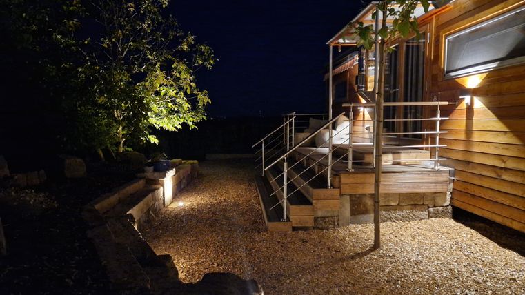 Ein modernes Gebäude bei Nacht mit sanfter Beleuchtung. Der Weg ist mit Kies und Pflanzen gesäumt, was eine einladende Atmosphäre schafft.